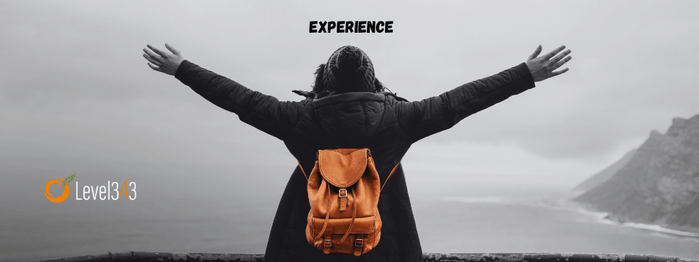 A woman stands in front of a beautiful view with arms spread wide. The word "experience" is written above her, showcasing the "experience" part of Google's E-E-A-T Quality Rater guidelines.