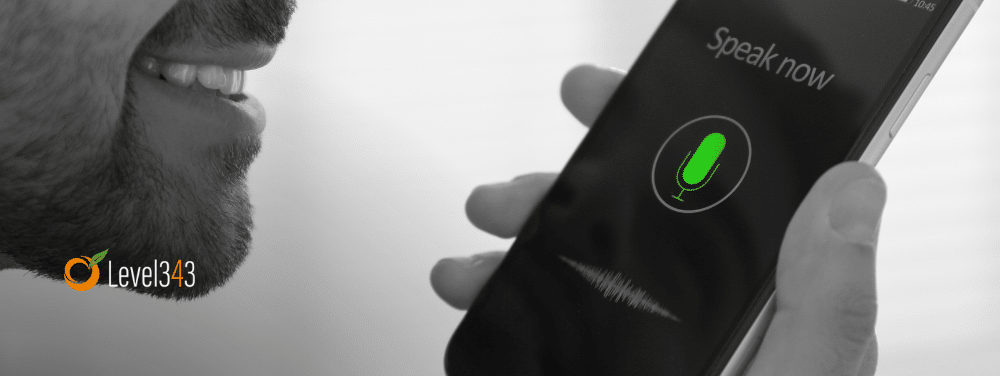 A hand holds a phone. A microphone shows on the screen, indicating the use of voice search