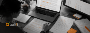 A black-and-white overhead desk scene shows a writer reviewing and marking up documents beside a laptop and analytics monitor, to make sure she is writing for humans. She's surrounded by notebooks, checklists, sticky notes, and a coffee mug.